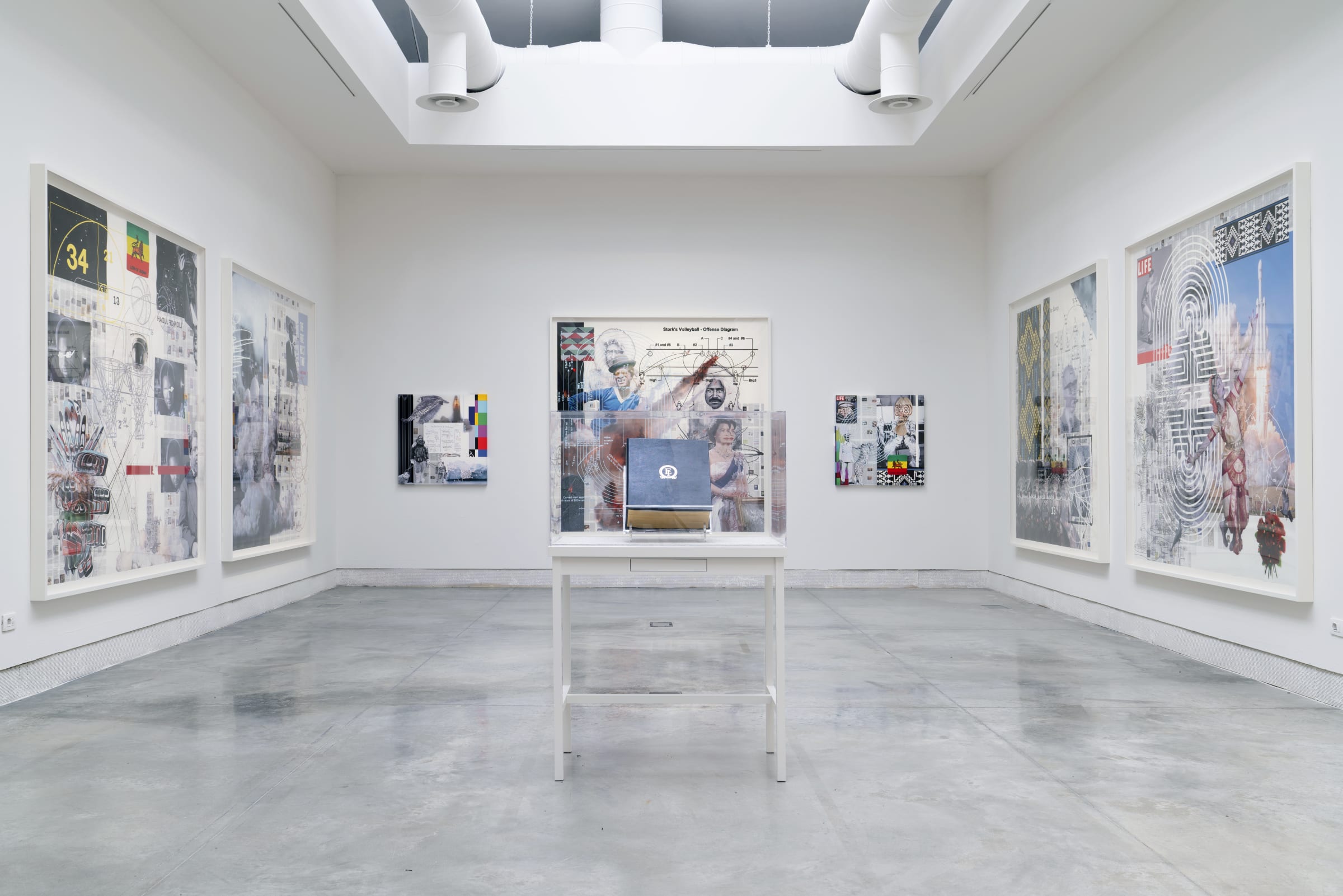 Installation view of various framed works on 3 walls with a vitrine in the center by Tavares Strachan